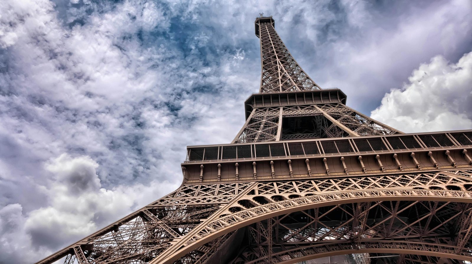 Dramatic low angle shot of the Eiffel Tower against a moody cloudy sky in Paris, France.